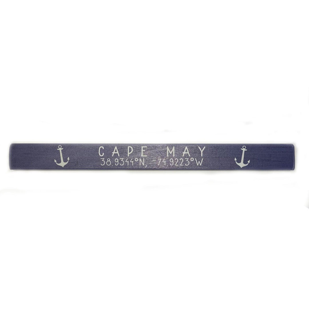 The Cape May Coordinates sign by SincereSurroundings, in navy blue wood, features "CAPE MAY 38.9341°N 74.9223°W" and small white anchors on each side, ideal for a nautical-themed shelf.