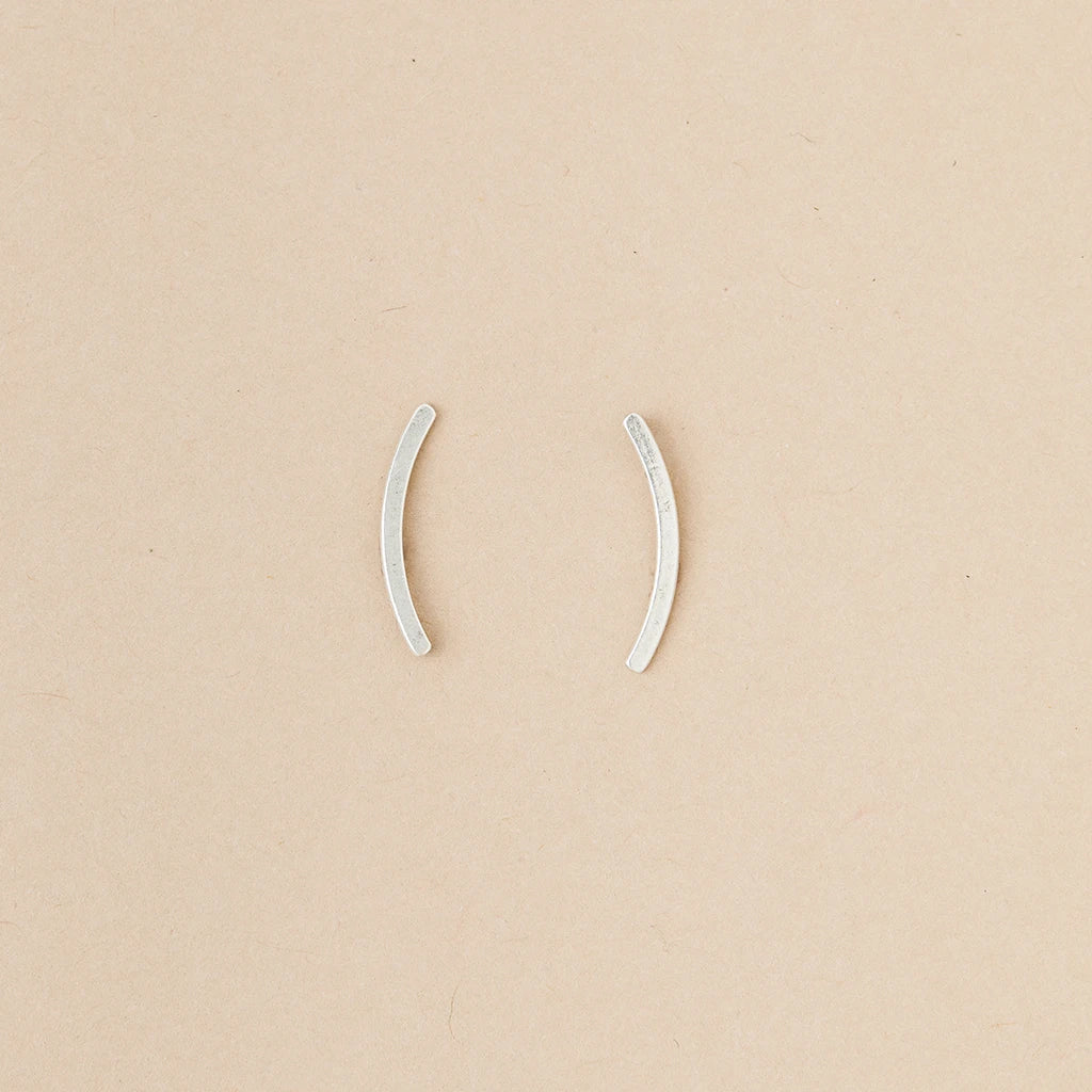 Part of Scout Jewelry's Comet Curve Silver collection, these two small, curved ear cuffs are elegantly displayed on a beige background.