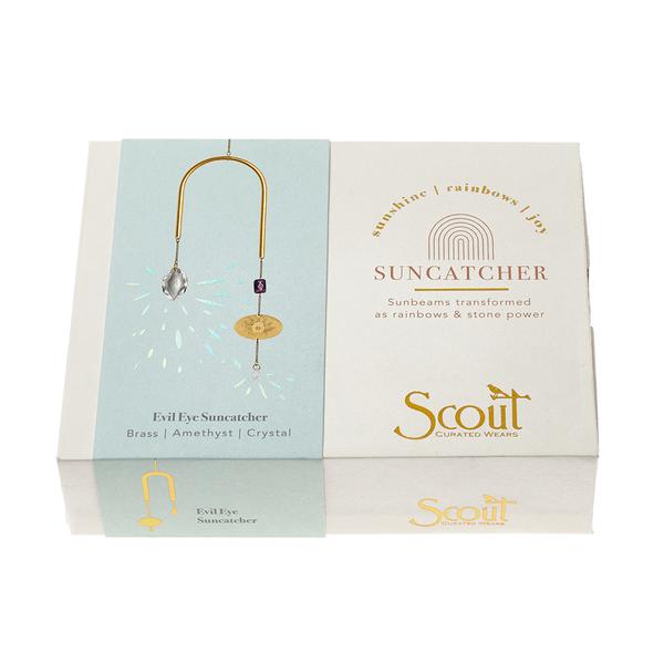 The Evil Eye Amethyst Suncatcher from Scout Jewelry features a brass design embellished with amethyst and crystal gems. Its packaging describes how sunbeams create vibrant rainbows, adding a magical touch to any space.
