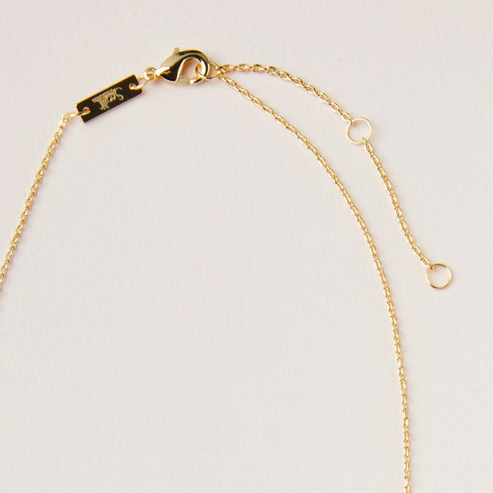 A close-up of the Scout Jewelry Intention Neck Labradorite/Gold necklace features a delicate gold chain with a lobster clasp and adjustable brass extender, all set against a plain light background, highlighting its simplicity and elegance.